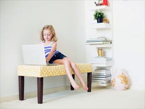 Girl (4-5) sitting on bench using laptop