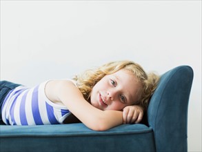 Portrait of girl (4-5) lying on bench indoors