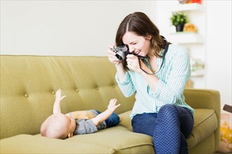 Mother sitting on sofa photographing baby boy (6-11 months)