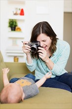 Mother sitting on sofa photographing baby boy (6-11 months)