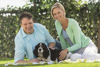 Couple with dog relaxing on grass.