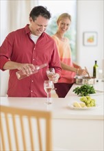 Couple cooking at home, man pouring wine.