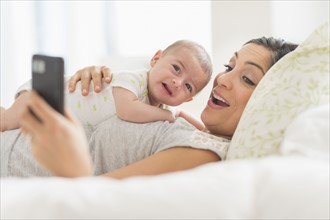 Mother photographing herself and baby boy (2-5 months) with cell phone.