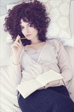 Portrait of beautiful brunette woman lying on bed with diary.