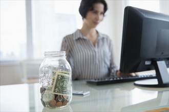 Money in jar on businesswoman's desk.
Photo : Jamie Grill
