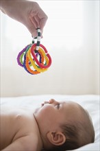 Hand holding colorful toy above baby girl (2-5 months).
Photo : Jamie Grill