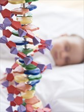 Baby girl (2-5 months) sleeping in bed behind DNA model.
Photo : Jamie Grill