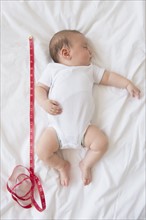 Baby girl (2-5 months) sleeping in bed with tape measure.
Photo : Jamie Grill