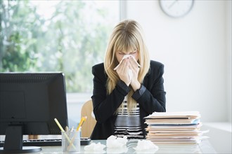 Businesswoman blowing nose in office.
Photo : Jamie Grill
