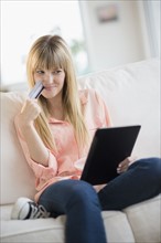 Woman sitting on sofa holding credit card and tablet pc.
Photo : Jamie Grill