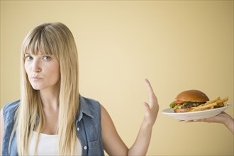 Portrait of woman rejecting hamburger that is being offered to her.
Photo : Jamie Grill