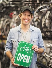 Portrait of man in bike shop holding open sign.
Photo : Daniel Grill