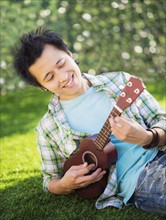 Teenage boy (16-17) playing guitar in park.
Photo : Daniel Grill