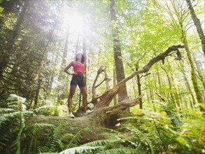 Young woman standing on log in forest. USA, Oregon, Portland.