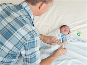 Father wrapping newborn son (0-11 months) in blanket.