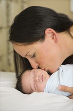 Portrait of mother kissing newborn baby (0-11 months).