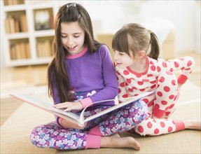 Two sisters (4-5, 8-9) reading picture book.