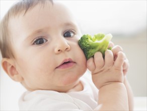 Baby girl (12-17 months) holding broccoli.