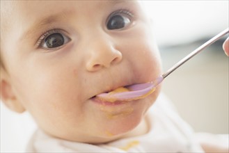 Close-up of baby girl (12-17 months) being spoon fed.