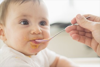 Close-up of baby girl (12-17 months) being spoon fed.