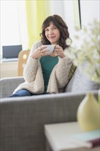 Portrait of woman sitting on sofa holding hot drink.