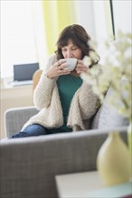Woman sitting on sofa holding hot drink.
