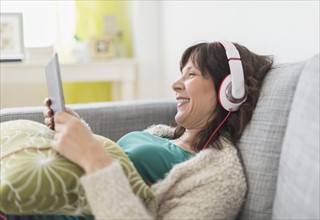 Woman relaxing on sofa, listening to music on tablet pc.