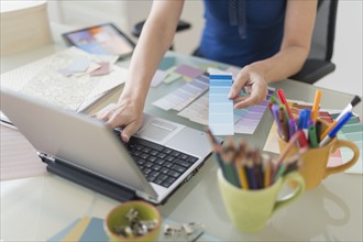 Woman holding color swatches and using laptop.