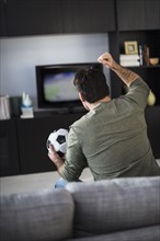 Rear view of man watching sports on tv.