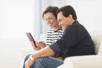 Couple sitting on sofa looking at digital tablet.