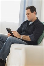 Man sitting on sofa looking at digital tablet.