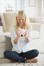 Portrait of young woman empting coins from piggy bank.
Photo : Jamie Grill