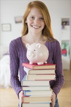 Portrait of girl (12-13) with books and piggy bank.
Photo : Jamie Grill