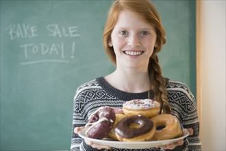 Portrait of girl (12-13) holding plate with doughnut.
Photo : Jamie Grill