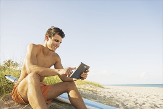 Young man sitting on beach with surfboard and digital tablet. Jupiter, Florida, USA.
Photo :