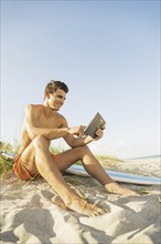 Young man sitting on beach with surfboard and digital tablet. Jupiter, Florida, USA.
Photo :