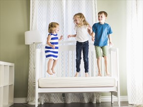 Girls (4-5, 6-7) and boy (8-9) jumping on sofa.
Photo : Jessica Peterson