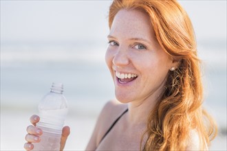 Portrait of woman drinking water on beach.