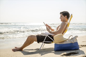 Side view of man sitting on deckchair and using digital tablet.