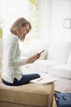 Woman sitting in living room and using digital tablet.