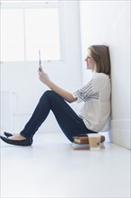 Young woman sitting on floor and using digital tablet.