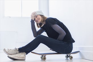 Young woman sitting on skateboard.
