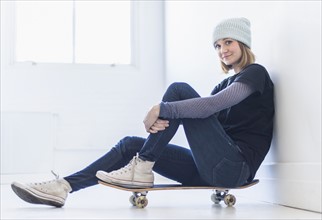 Portrait of young woman sitting on skateboard.