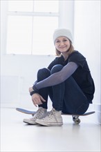 Portrait of young woman sitting on skateboard.
