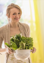 Portrait of young woman holding lettuce in colander.