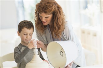 son (6-7) and mother changing lightbulb in table lamp.