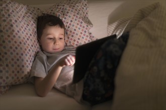 boy (6-7) using digital tablet in bed.