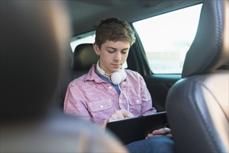 Teenage boy (16-17) using digital tablet in car.
