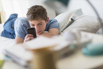 Teenage boy (16-17) lying on bed and text messaging.