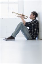 Teenage boy (16-17) playing trumpet in hallway.